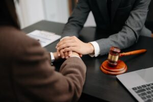 Business professionals compassionately holding hands while discussing contract papers with a laptop and tablet in an office setting.