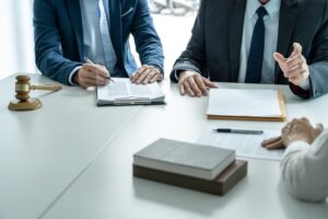 Businesspeople and a male lawyer hold a team meeting with a client at a law firm office, discussing legal services.