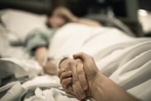 Ill woman lying in a hospital bed with a loved one holding her hand. Concept of family support and medical challenges.