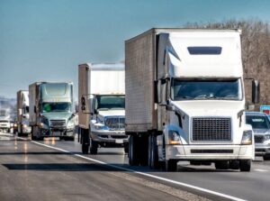 Horizontal view of a convoy of eighteen-wheeler trucks traveling on an interstate highway.