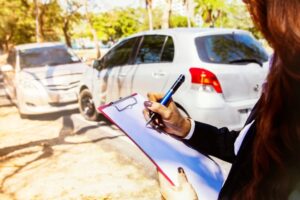 A female insurance agent at a car crash scene takes notes and gathers evidence to assist with insurance claims and resolve disputes between involved parties.