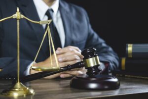 Legal consultation: judge's gavel, scales of justice, and lawyer advising with documents at courtroom desk.