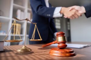 Professional lawyer handshake in meeting with justice scales and gavel on desk, symbolizing legal agreement