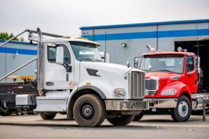 Two skid-mounted big rigs, day cab semi trucks, parked closely in a warehouse lot, ready for waste container transport orders.