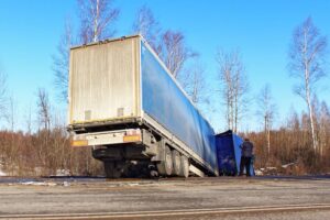 Tilted and wrecked Amazon semi-truck in a roadside ditch on a sunny spring day, on a suburban highway.