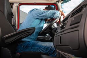 Side view of a fatigued truck driver resting on the steering wheel inside the vehicle cabin after finishing their route.