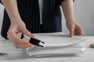 Close-up of a woman attaching documents with a metal binder clip on a white wooden office desk.