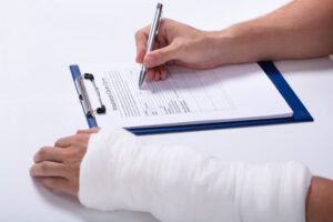 Person's hand filling out a health insurance claim form on a white desk.