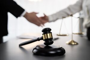 Close-up of a gavel symbolizing justice, with blurred background of lawyers shaking hands after a successful legal deal.