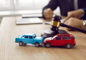 Little crashed autos on table in courtroom. Gavel and two small toy car models on desk in courthouse. Concept of lawyer services, civil court trial, vehicle accident case study, and insurance coverage