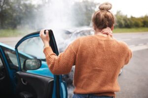 Rear view of an injured female motorist with a head injury stepping out of her car after a crash.